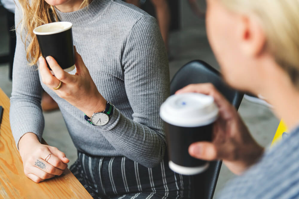 Deux personnes partageant un café lors d'une pause, symbolisant un moment de détente et de discussion entre parents.