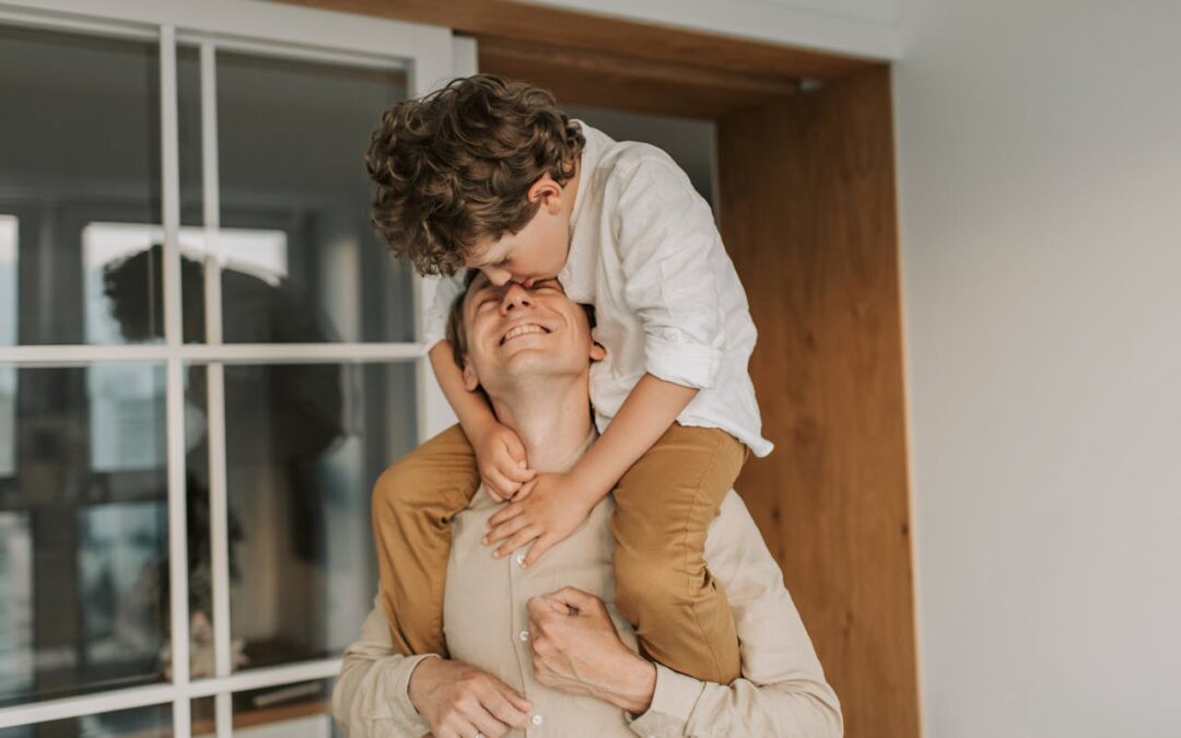 Un père portant son fils sur ses épaules, partageant un moment de tendresse à la maison.
